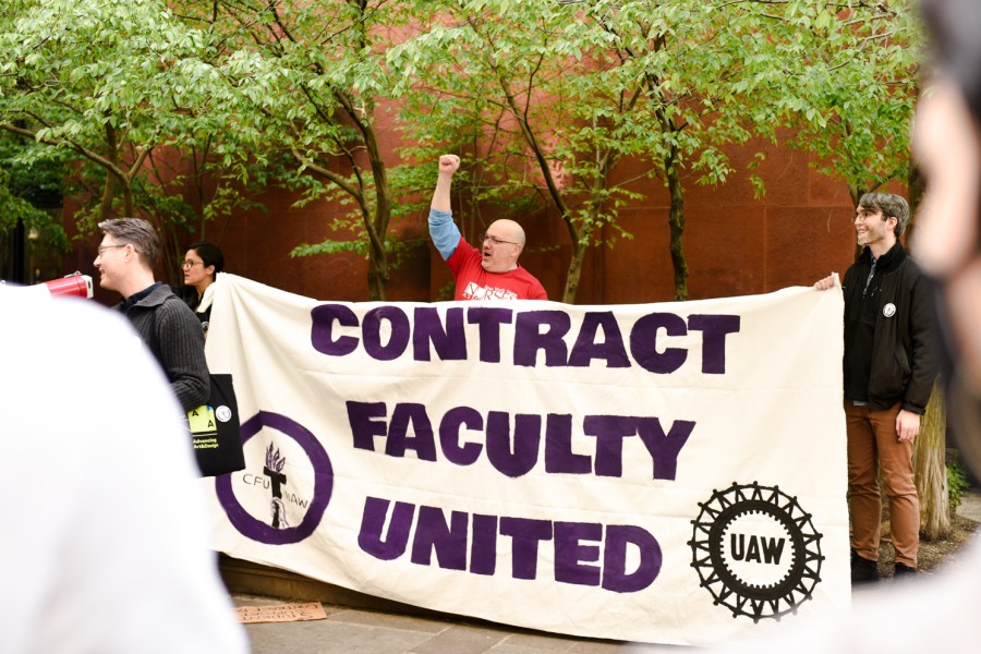 Three+people+hold+a+banner+that+reads+%E2%80%9CContract+Faculty+United.%E2%80%9D+One+of+them+has+his+fist+raised+in+the+air.