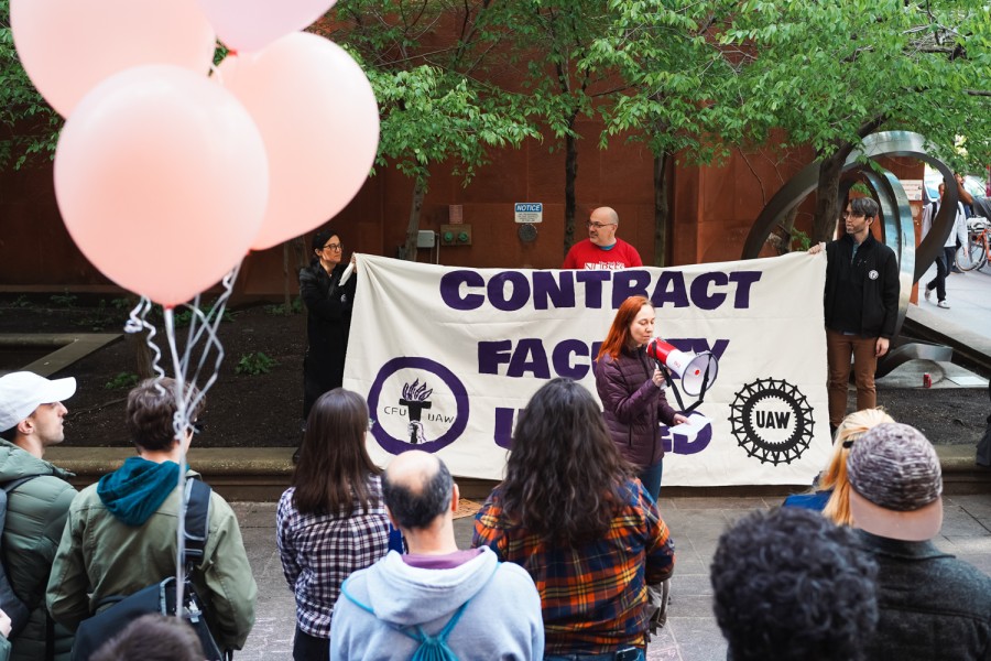 Three people hold a banner that reads “Contract Faculty United” behind a person speaking through a megaphone. A crowd stands around them.