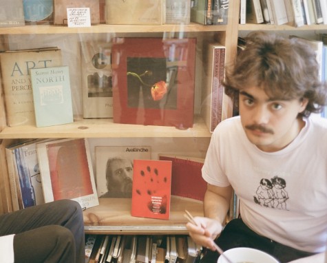 A photo of Nicolas Pedrero-Setzer eating ramen against a bookshelf.