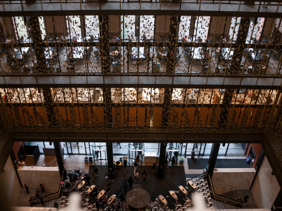 A photograph looking down on the Bobst Library atrium from a higher floor. On each level, metal barriers run from floor to ceiling.