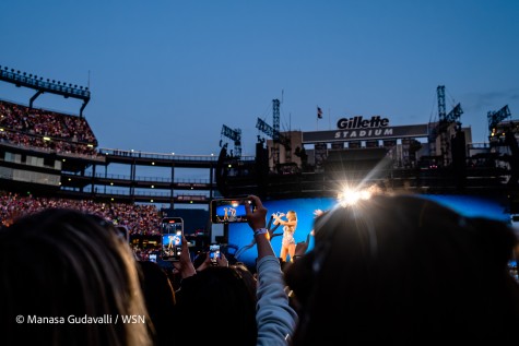 Concert attendees hold up their phones to record Taylor Swift’s performance. In the background is a sign that reads “Gillette Stadium”