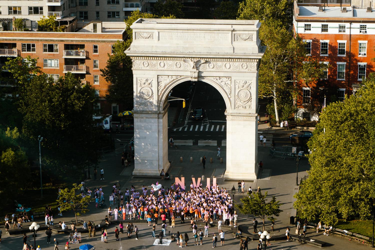 An aerial view of the Washington Square Arch with a crowd of NYU students wearing purple outfits in the background and holding up giant NYU letters.