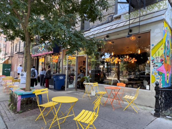 Sidewalk view of a storefront with outdoor seating and multiple “7.8.7. Coffee” signs.