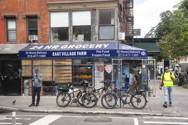 The exterior of East Village Farm and Grocery with bikes racked by it. The store sign is blue and white, and there are people standing on the two sides of the store.