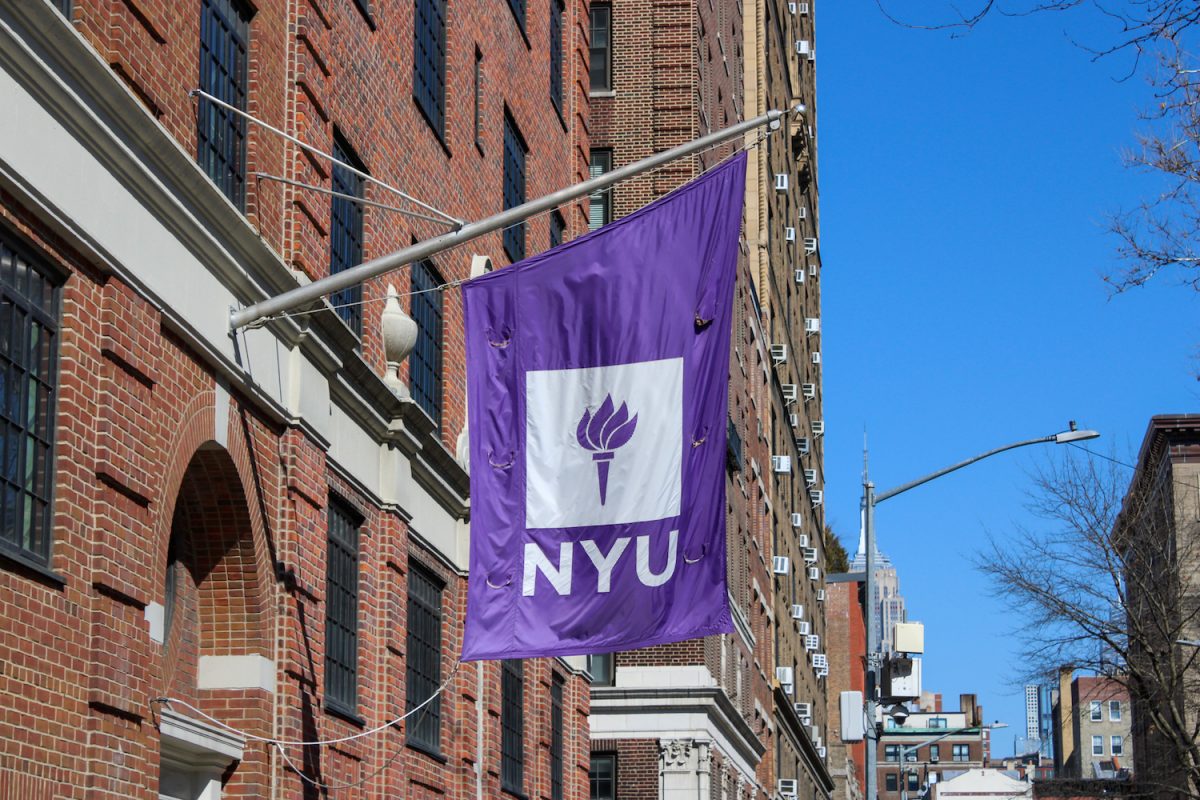 A flag with N.Y.U.’s logo hangs from a red brick building.
