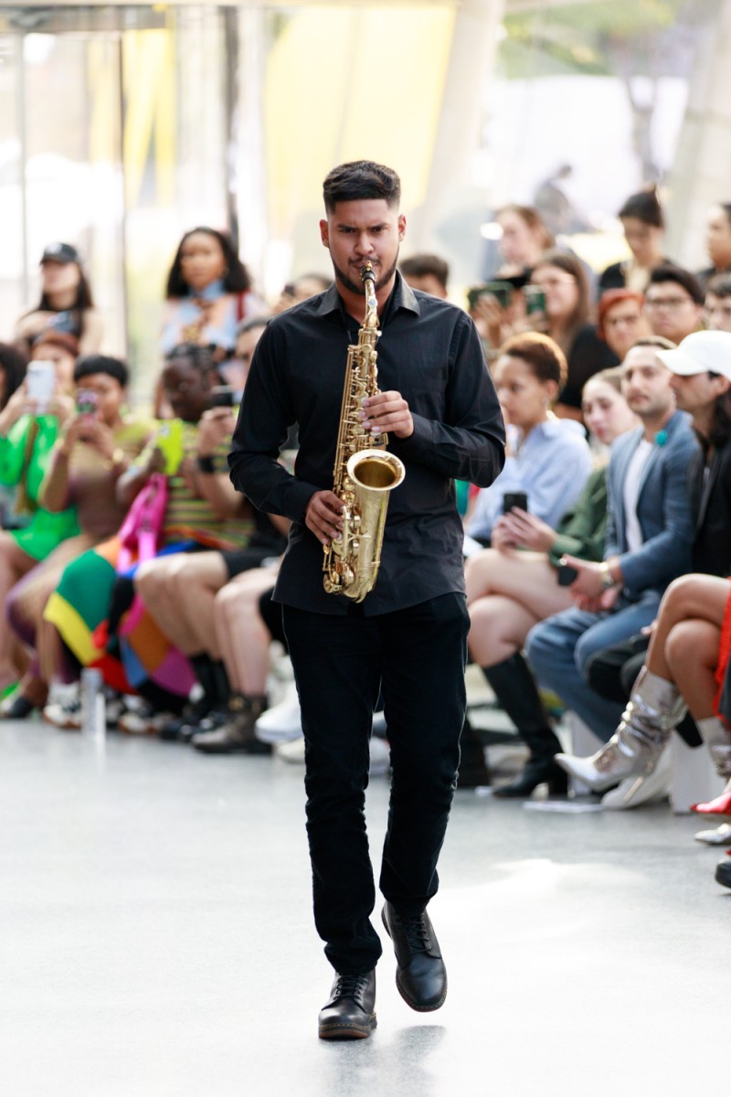 Marvin Carter plays a saxophone wearing a all-black suit.