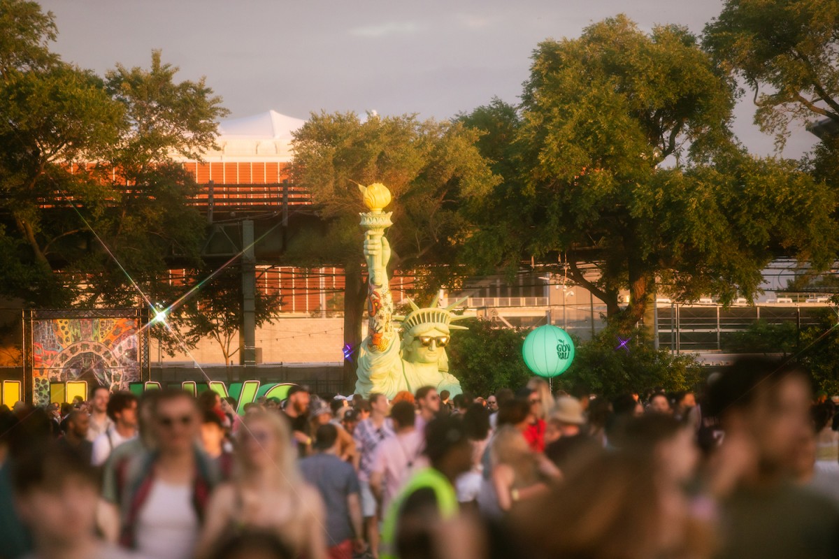 A crowd gathering at the Governors Ball music festival. There is a modified Statue of Liberty behind the crowd wearing a pair of sunglasses.
