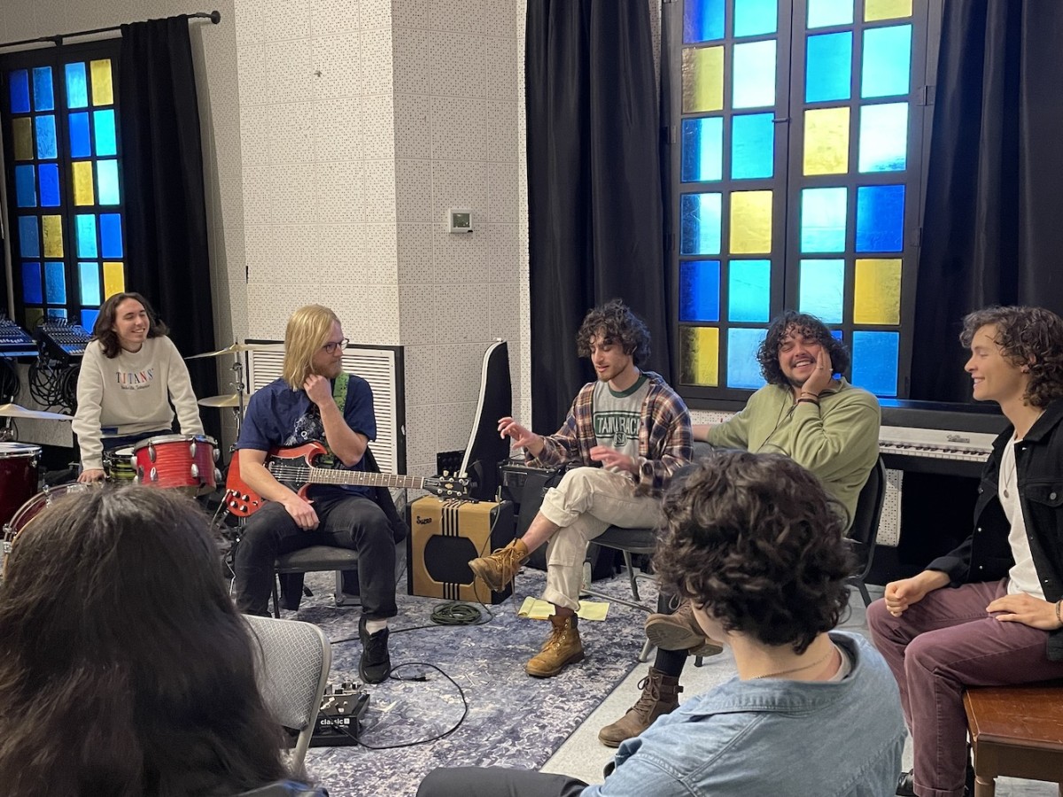 A group of students sitting in a circle, surrounded by various musical instruments including a keyboard and drum set.