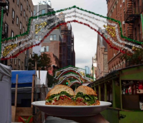 A sandwich from Rubirosa on a plate held up on a street in Little Italy