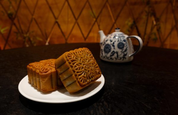 Two mooncakes are on a plate, sitting on a table. To the left of the photo there is a blue-and-white teapot.