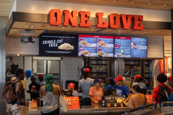 Customers ordering from the counter in the restaurant Raising Cane’s. The words “One Love” are above the counter.