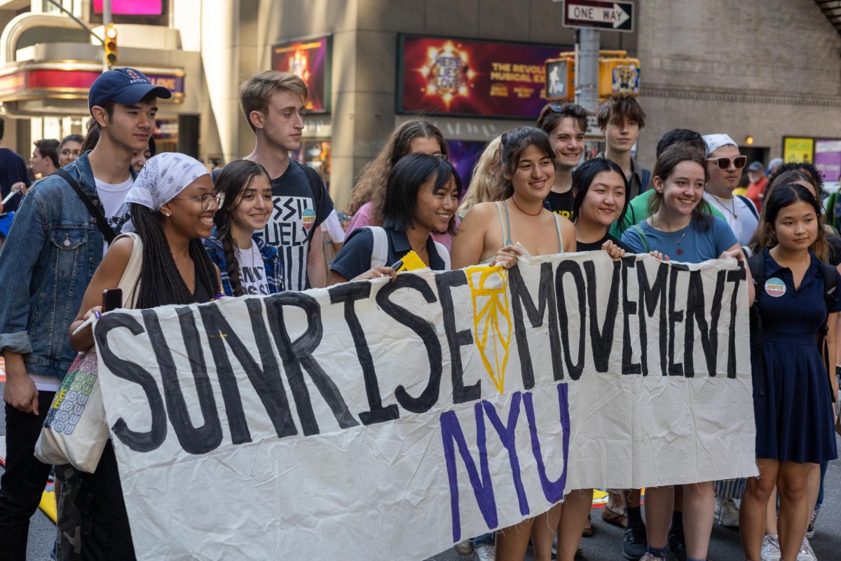 A group of about 15 students holding a sign reading “Sunrise Movement N.Y.U.”