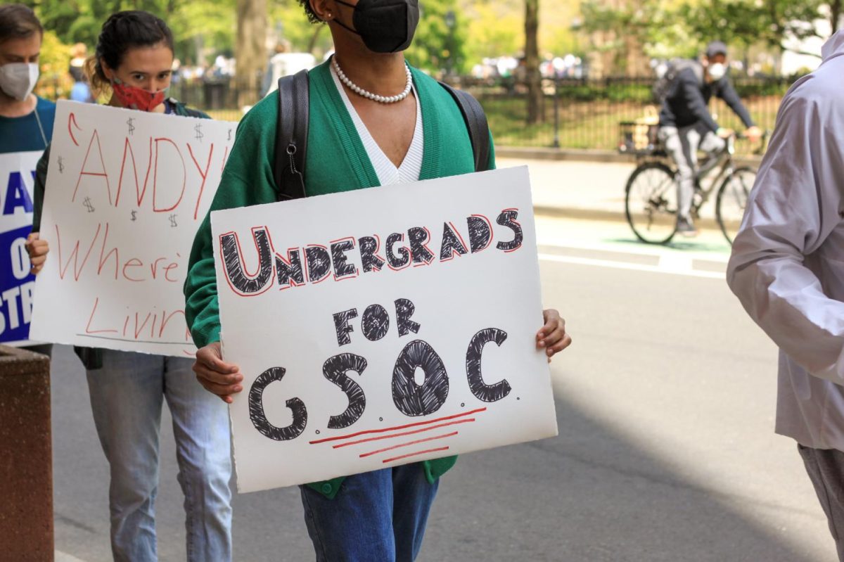 A protester wearing a green sweater and a pearl necklace is holding a sign that says ‘Undergrads for GSOC.
