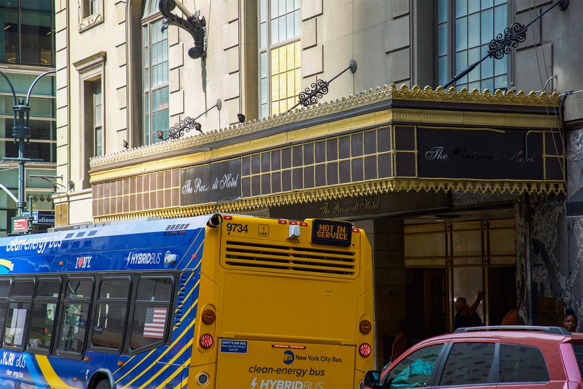 The entrance to The Roosevelt Hotel in New York City with a bus on the street in front of it.