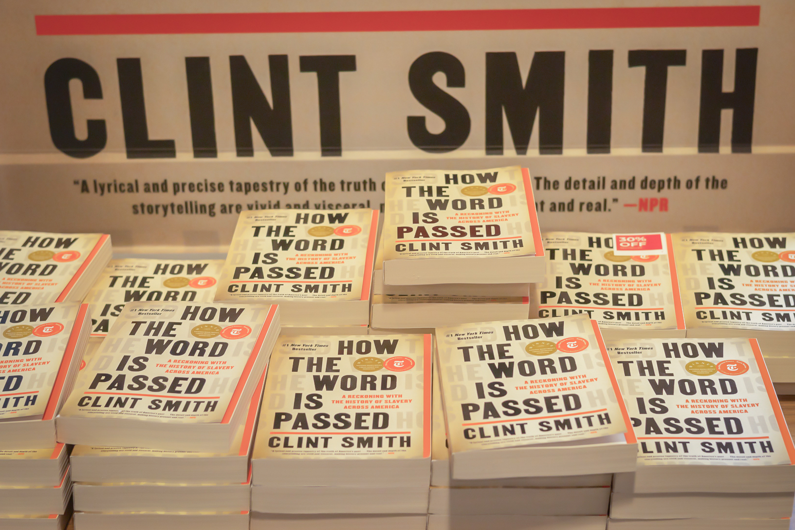 A pile of Clint Smith’s book “How the Word is Passed” displayed in the N.Y.U. Bookstore. Behind the pile is a board with Smith’s name written on it.