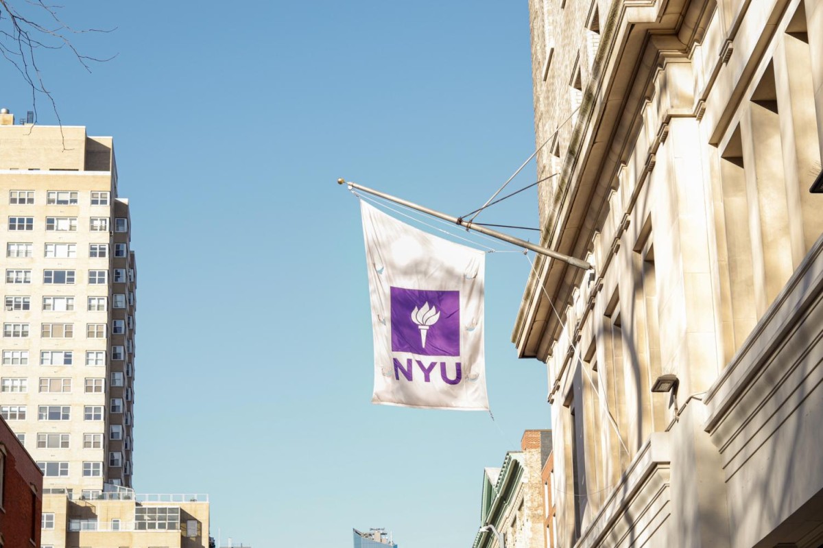 A white banner with purple letters that read N.Y.U. and a symbol of a torch hangs from the facade of The Silver Center of Arts and Science.