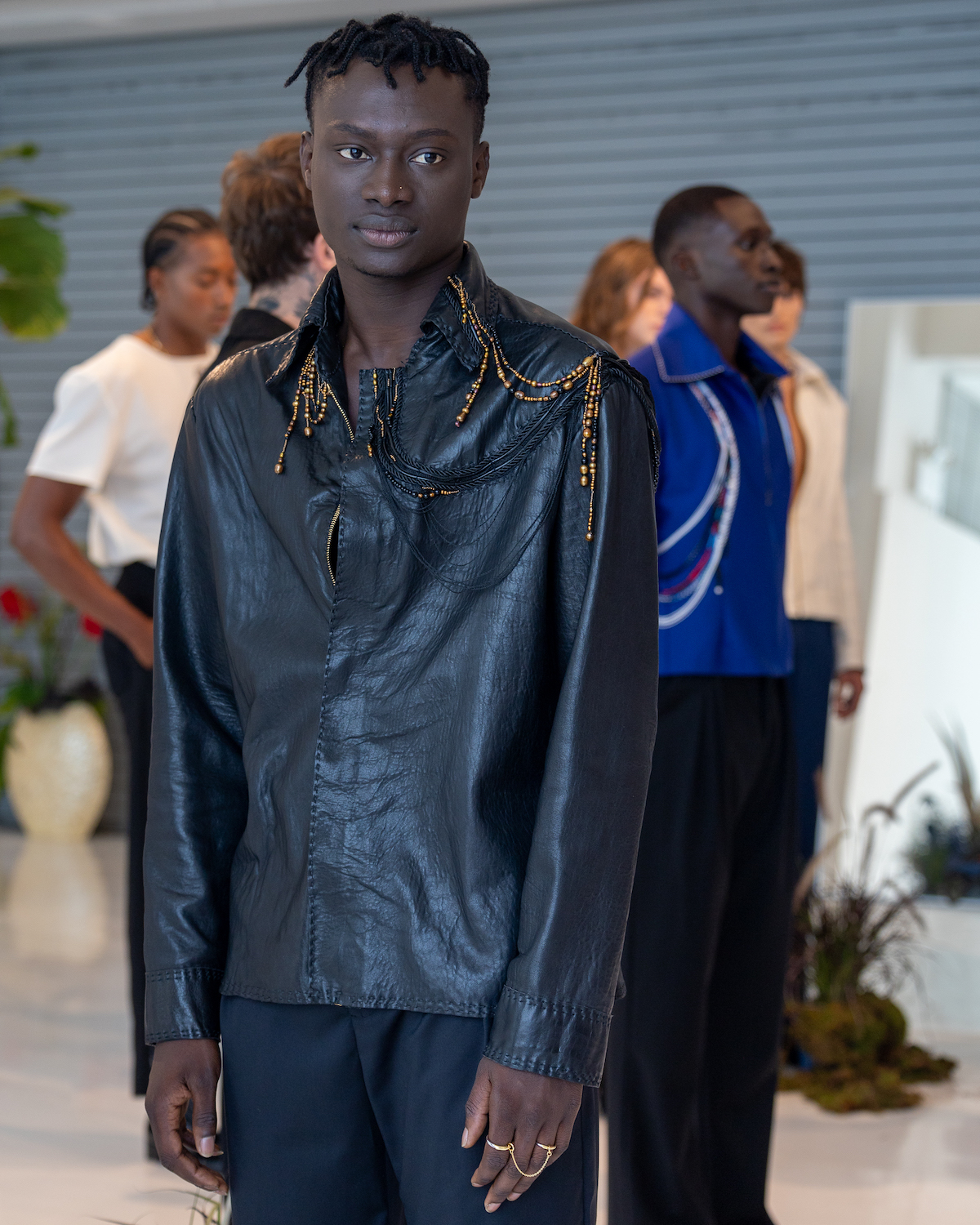 A model wearing a black outfit with gold hardware stands in the middle of the room. The model is wearing clothes from KENT ANTHONY.