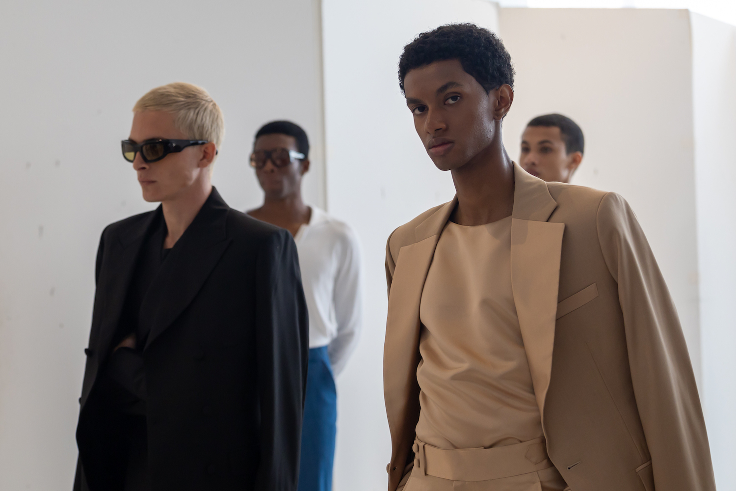 Four models stand in two lines in a white showroom. The models are wearing clothes from B.M.C.