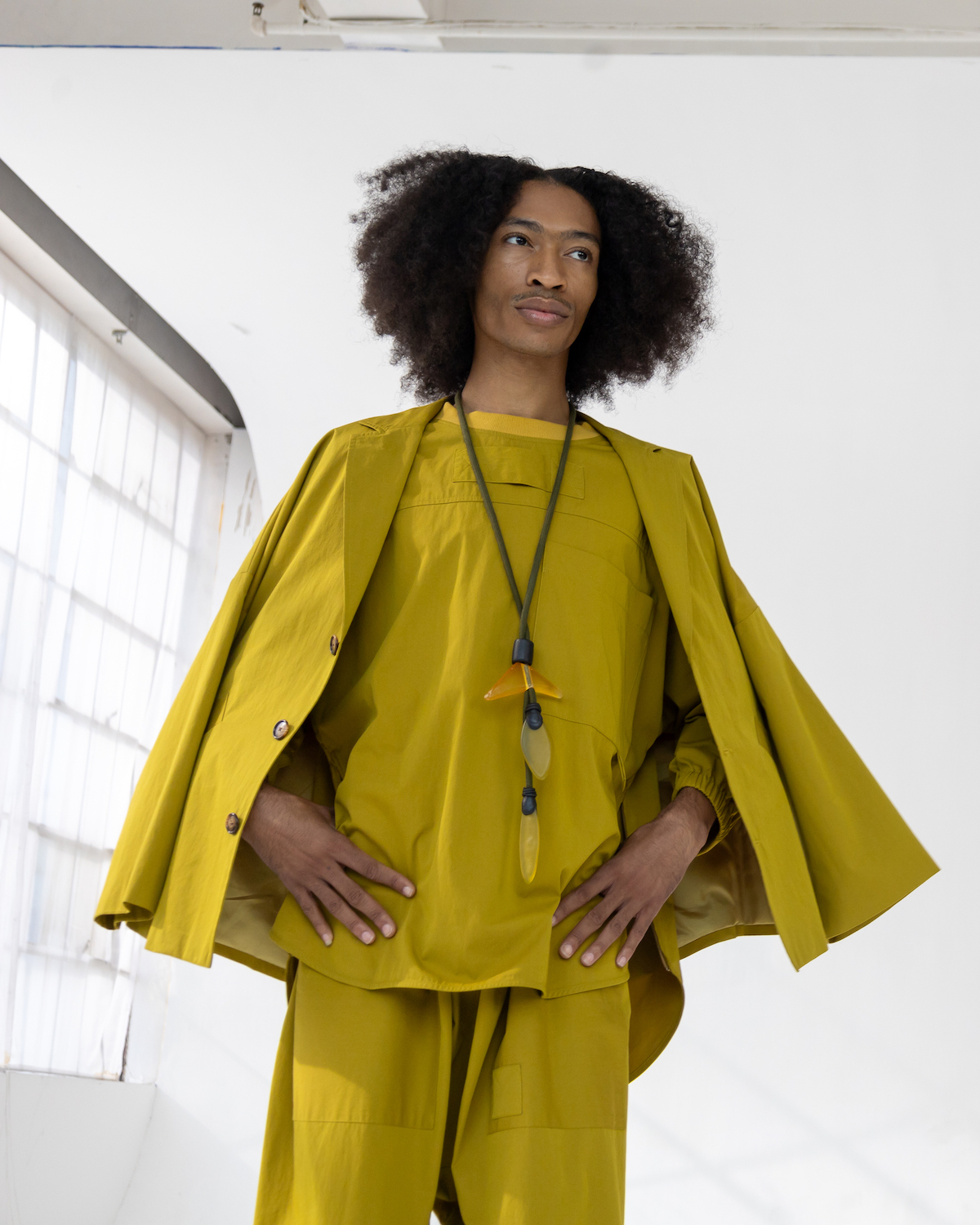 A model wearing a mustard outfit stands after walking down a short runway. The model is wearing clothes from A.POTTS.