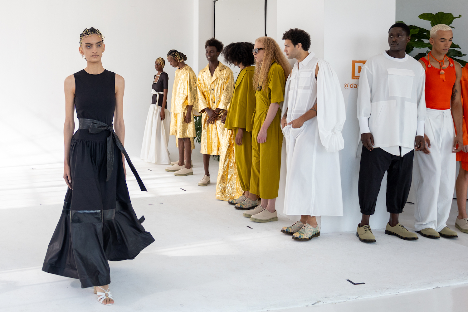 A model wearing a black dress walks down a short runway. The model is wearing clothes from A.POTTS.