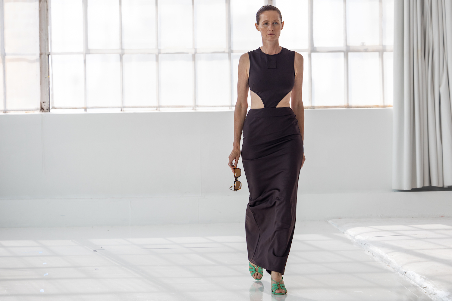 A model wearing a dark brown dress with teal shoes walks down a small runway. The model is wearing clothes from A.POTTS.