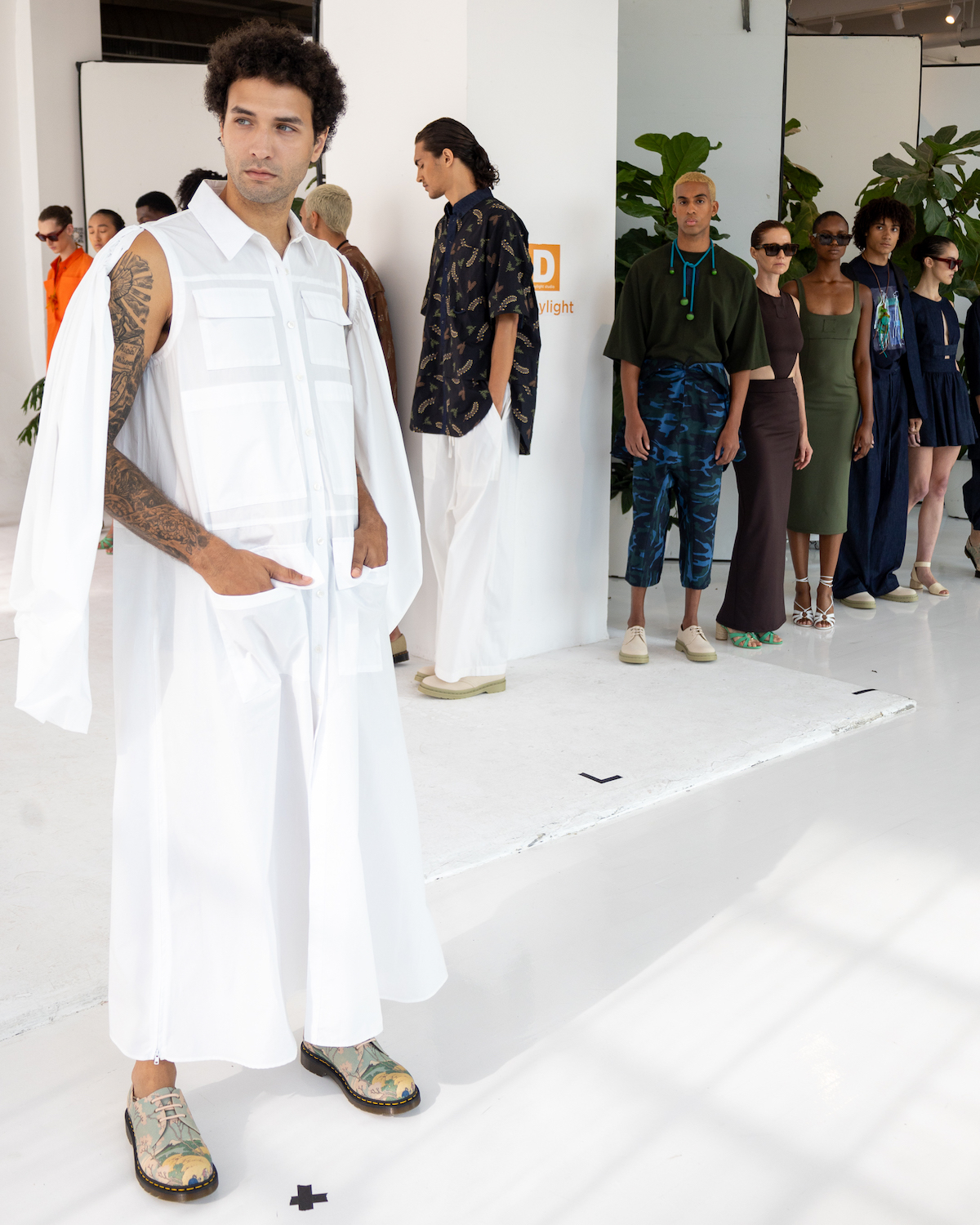 A model wearing a white outfit poses after walking down the short runway. The model is wearing clothes from A.POTTS.