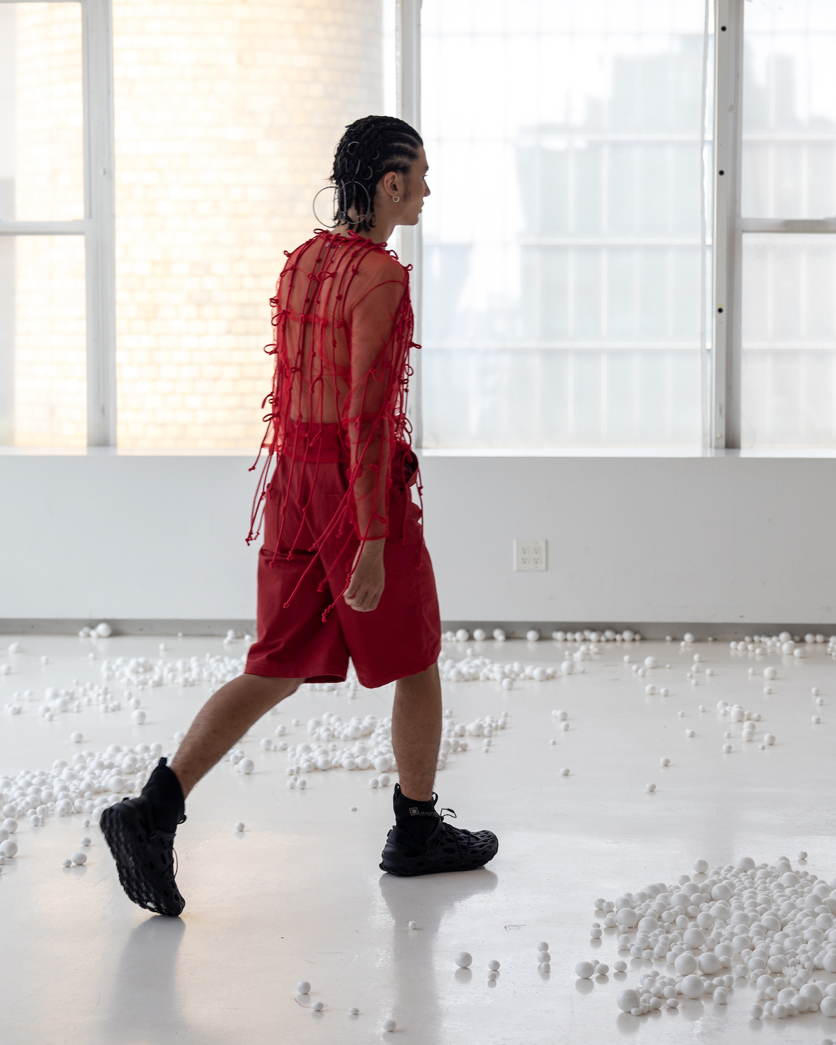 A model wearing a red mesh top and red shorts walks away from the camera. The model is wearing clothes from CLARA SON.