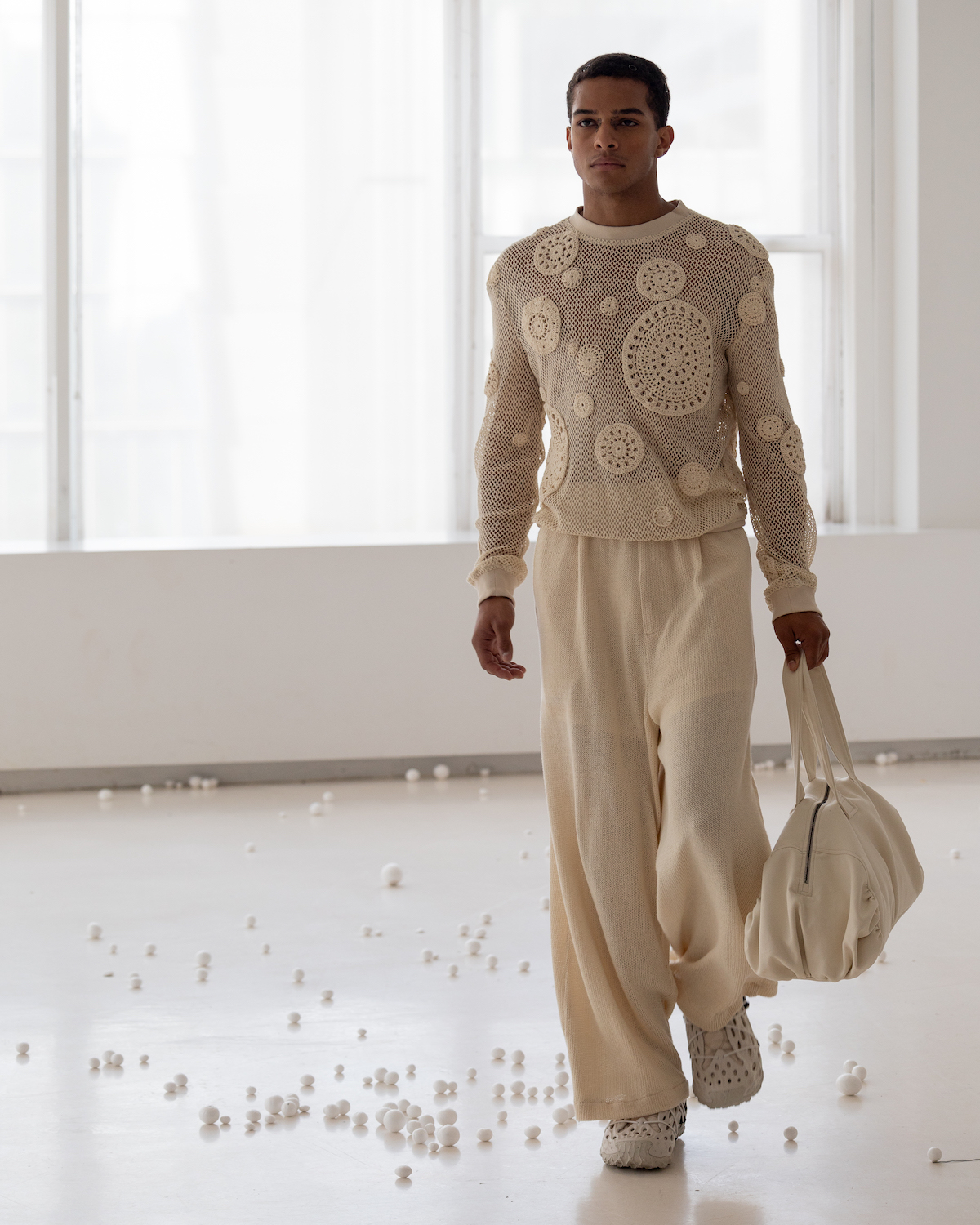 A model wearing a cream outfit with a cream bag walks towards the camera. The model is wearing clothes from CLARA SON.
