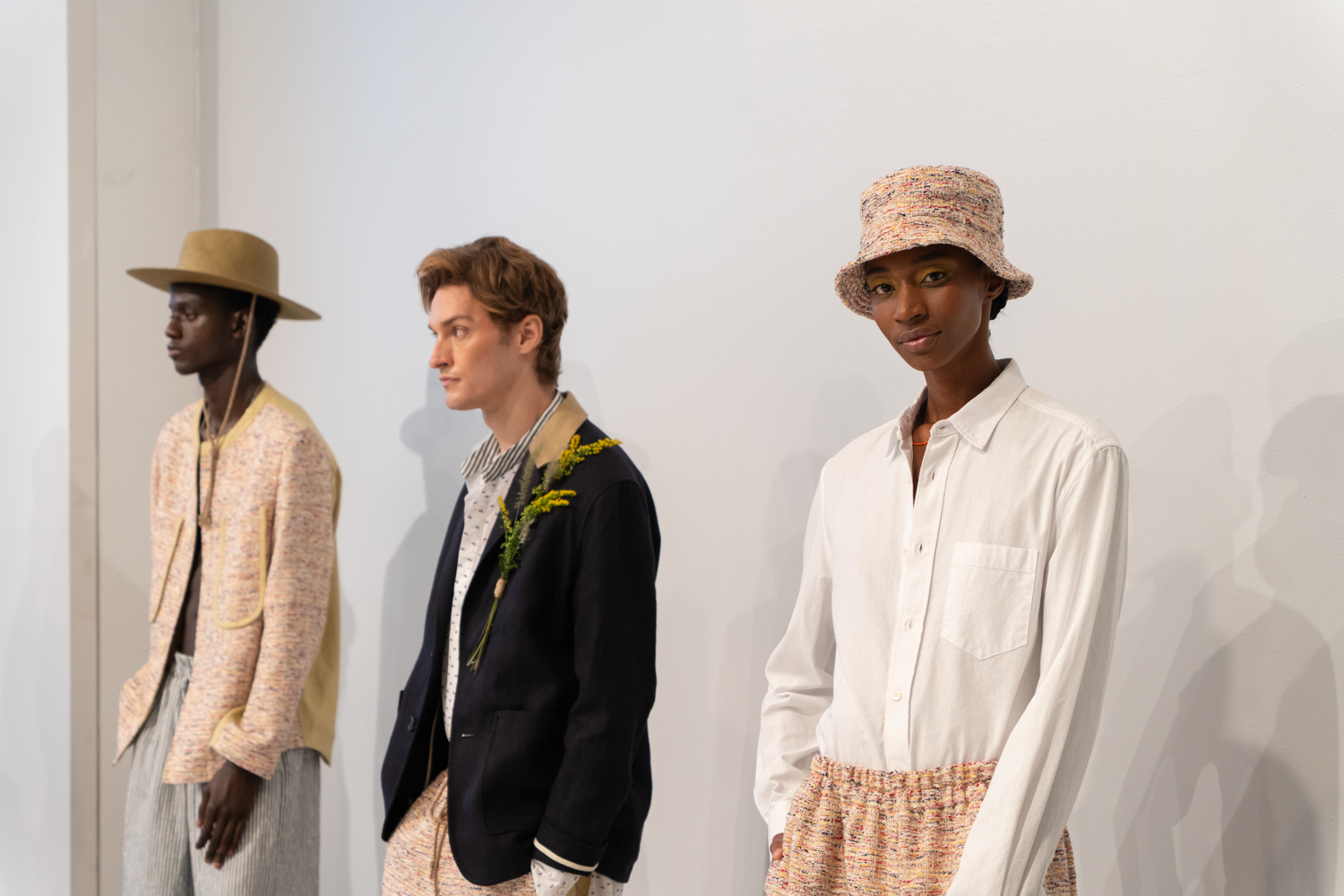 Three models stand in a fashion showroom with white walls. They are wearing clothing from the brand thesalting. The model on the right is looking and smiling at the camera.