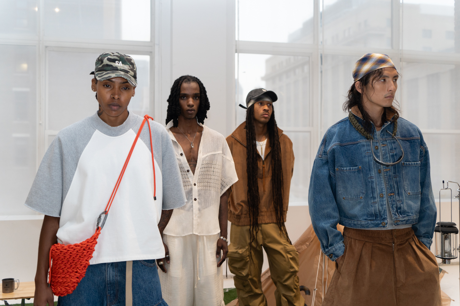 Four models stand in a fashion showroom with white walls. They are wearing clothing from the brand SEBASTIEN AMI.