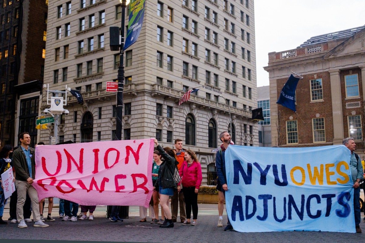 Protesters walk down University Place holding large signs that read ”N.Y.U. OWES ADJUNCTS” and “UNION POWER.”