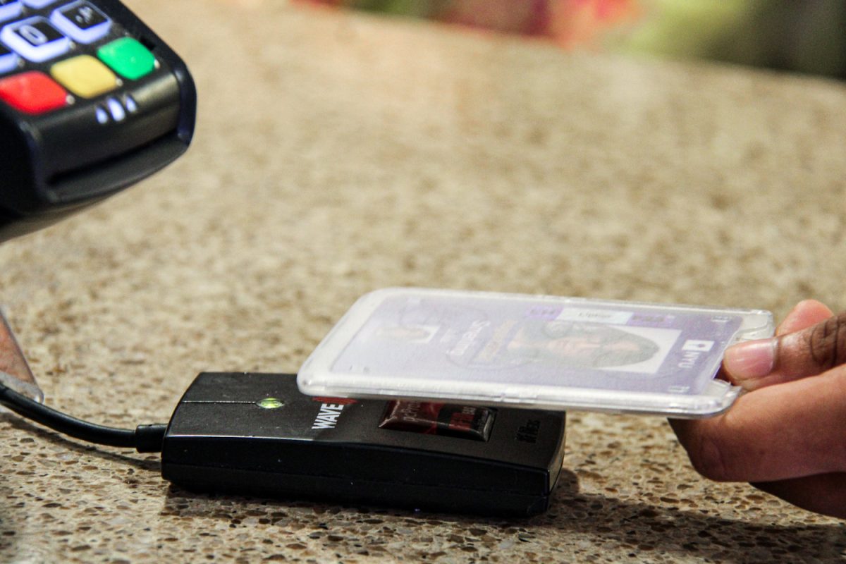 The close-up shot of a hand scanning an NYU ID card above a card reader.