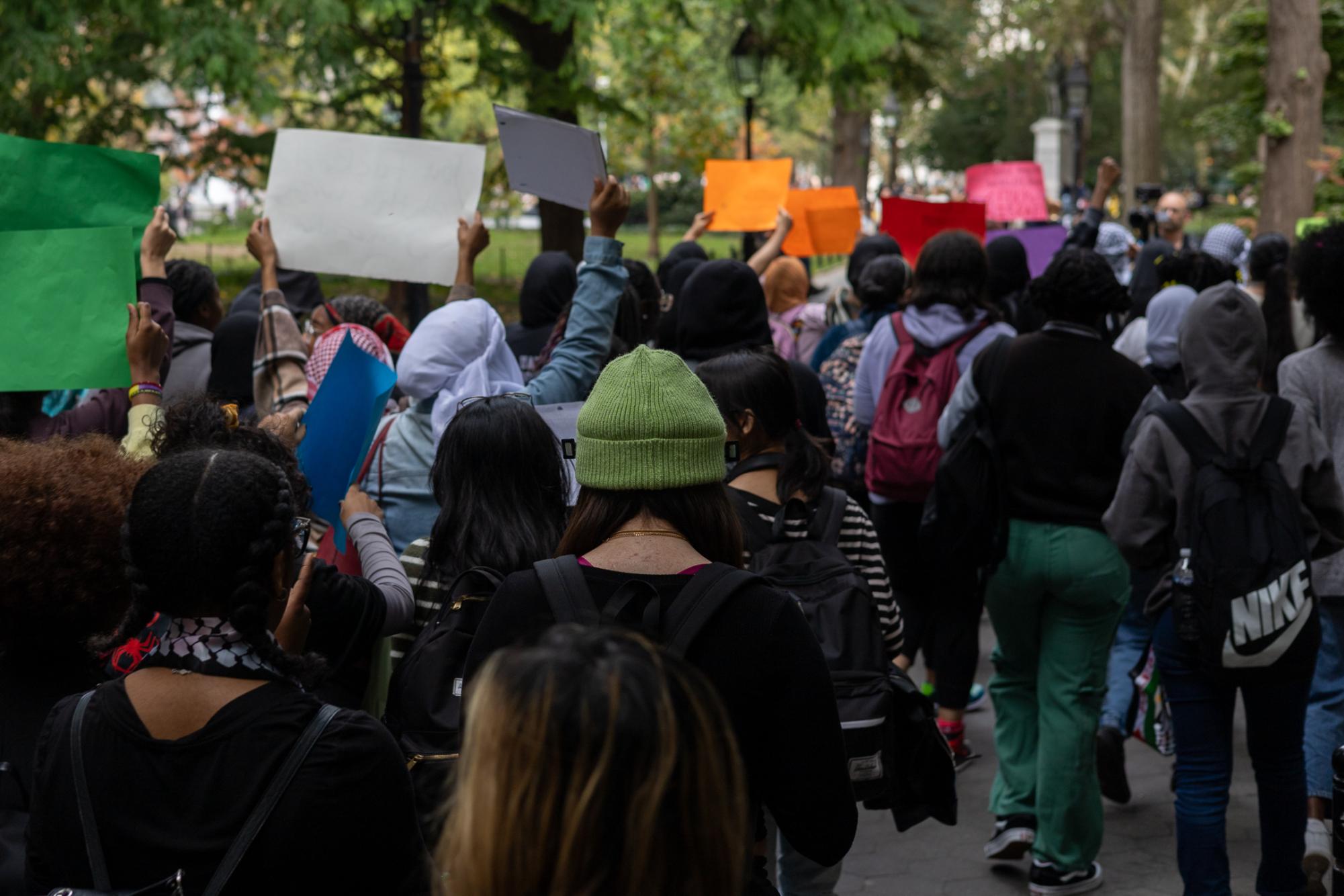 A crowd of people holding up signs while marching through Washington Square Park.