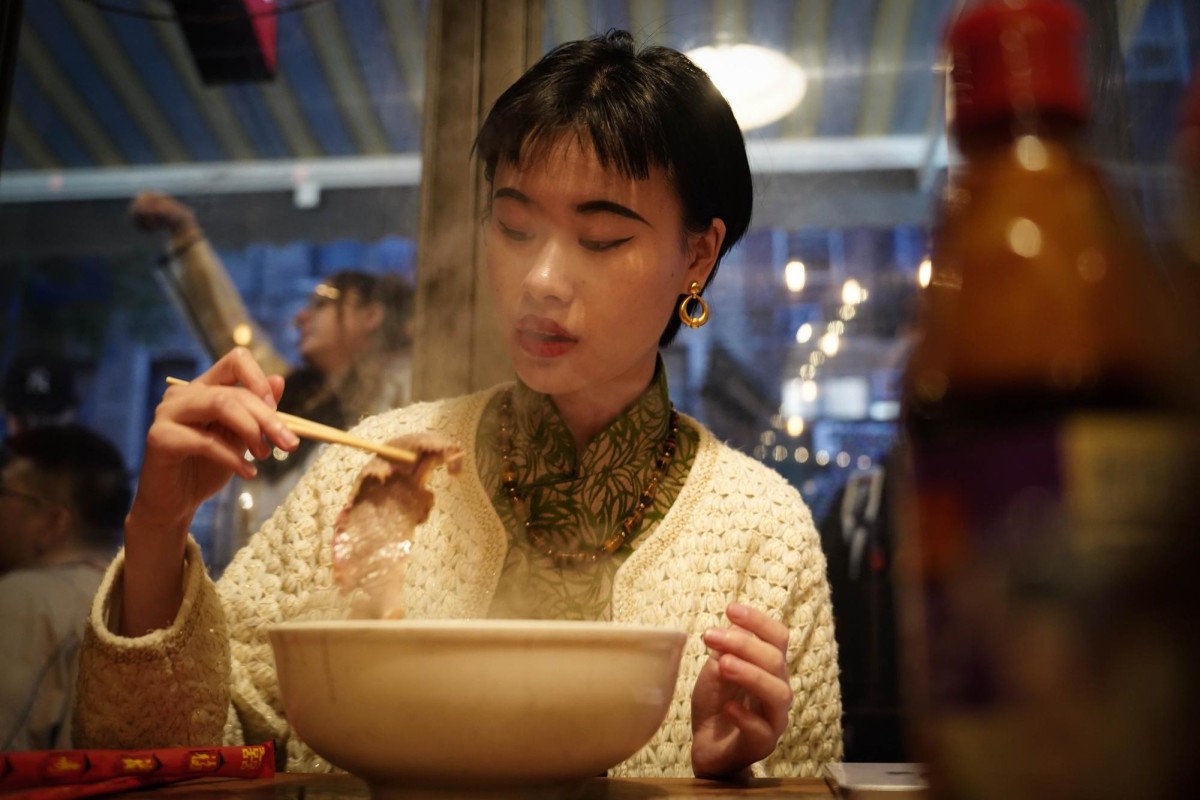 Heather Guo picks up a beef from a steaming bowl with a pair of chopsticks in a restaurant.
