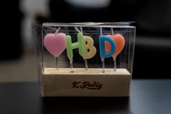 Pink, green, yellow, blue and orange candles placed side by side to form the letters “H.B.D.” with hearts on each side.