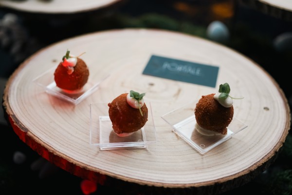 Three pieces of arancini on a wooden plate with cream on top of each.