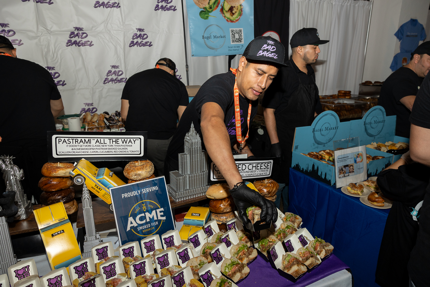 A man wearing a black hat and black shirt with purple accents stands behind a display table.