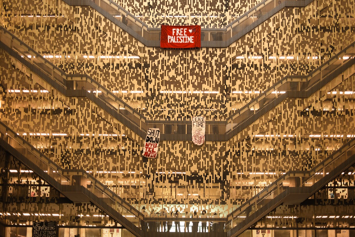 Three banners, each reading “Free Palestine,” “Shut Down N.Y.U. Tel Aviv” and “Cease-fire and De-cccupy,” hang from the staircases in the Bobst Library.