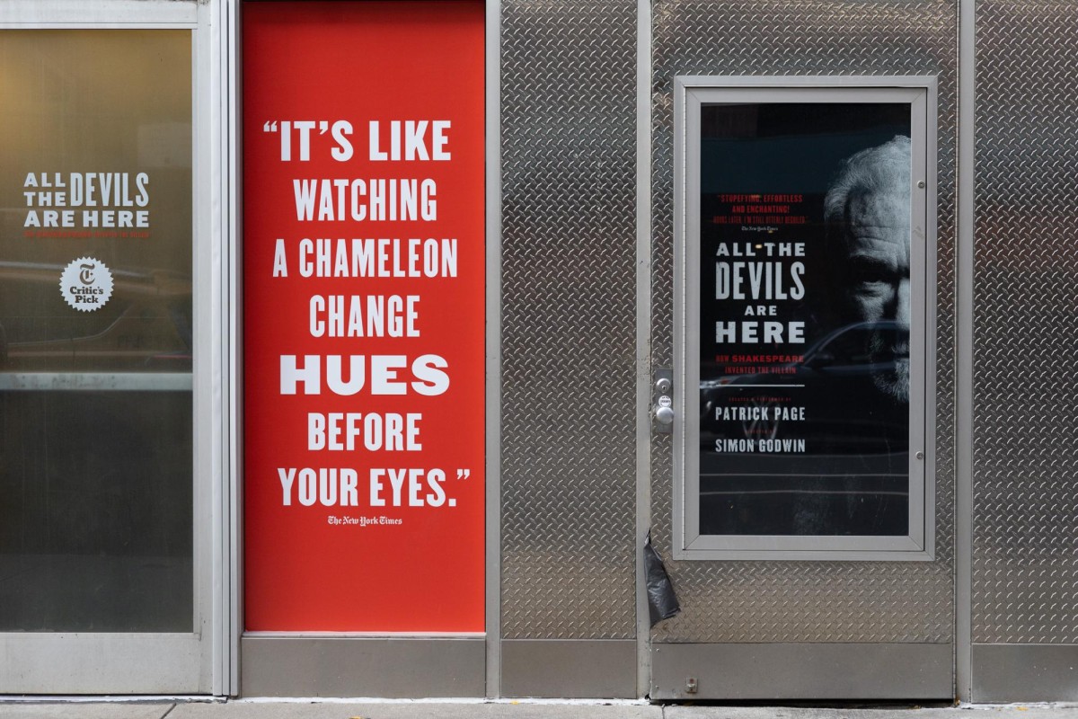 Two posters, a red one with white text printed on it on the left, and a black one with red and white texts and a black and white portrait on the right, is posted on the entrance of a theater.