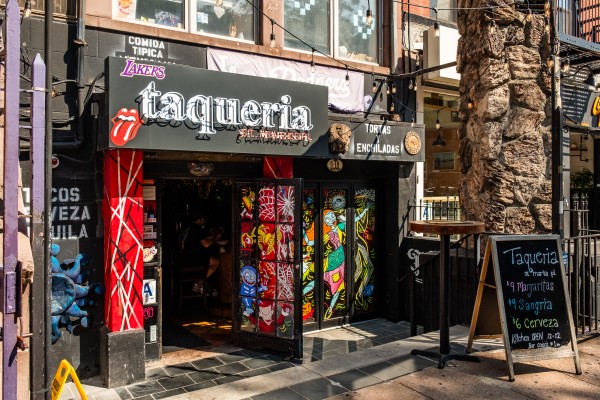 The entrance to a restaurant with colorful painted doors. A sign reads “Taqueria St Marks Place”.