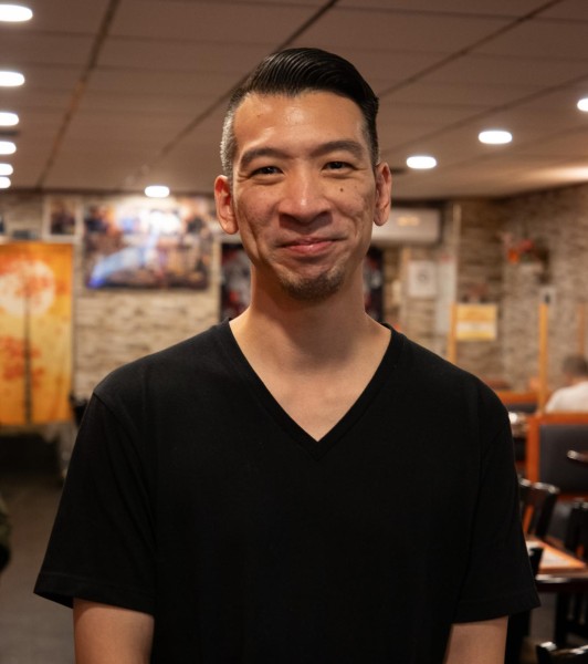 A man in a black t-shirt is standing and smiling, posing inside the restaurant.
