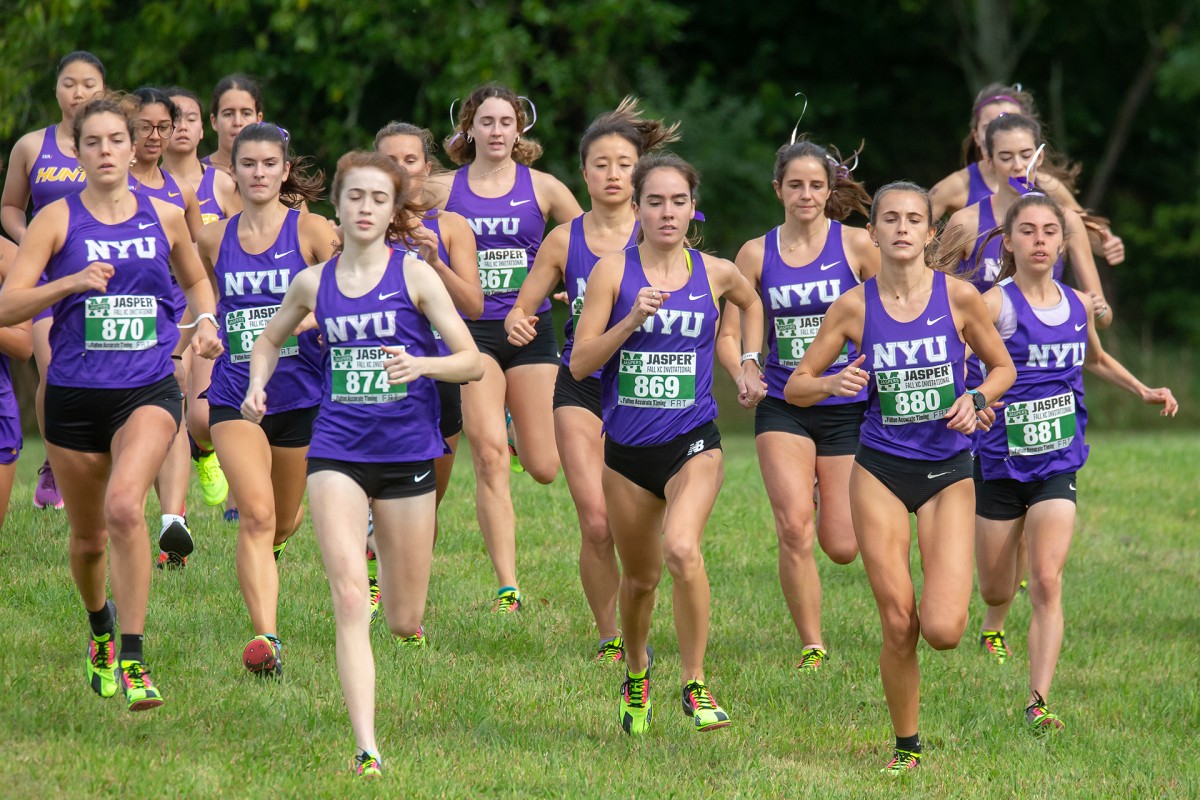 A line of women in purple pinnies and black shorts running on grass.