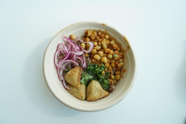 A bowl containing onions, chickpea stew, cilantro and samosas.