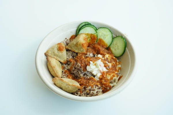 A bowl containing brown rice, cucumbers and samosas.