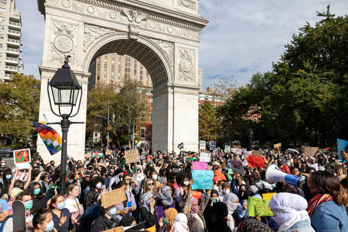 A+crowd+of+dozens+of+people+standing+underneath+the+Washington+Square+Park+arch+holding+various+colored+signs+and+flags+in+a+large+mass.