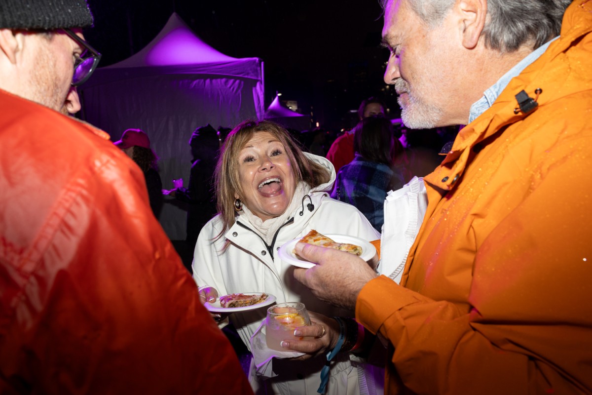 A woman in a white rain jacket smiles at the camera while holding a taco on a plate.