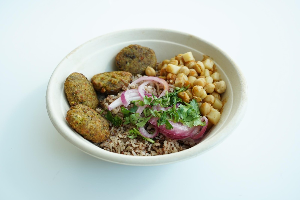 A bowl containing tikkis (potato patties), brown rice, cilantro, onions, and chickpeas.