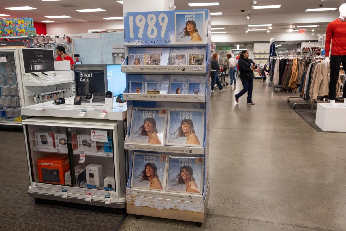A display of shelves showing Taylor Swift smiling with the words 1989 (Taylors Version) with multiple vinyls in the middle of a large room with other aisles of items on sale.