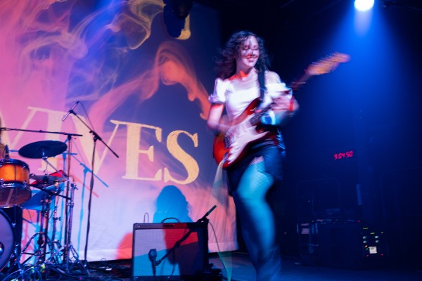 A woman plays guitar onstage. She is in motion, and her figure is slightly blurred.