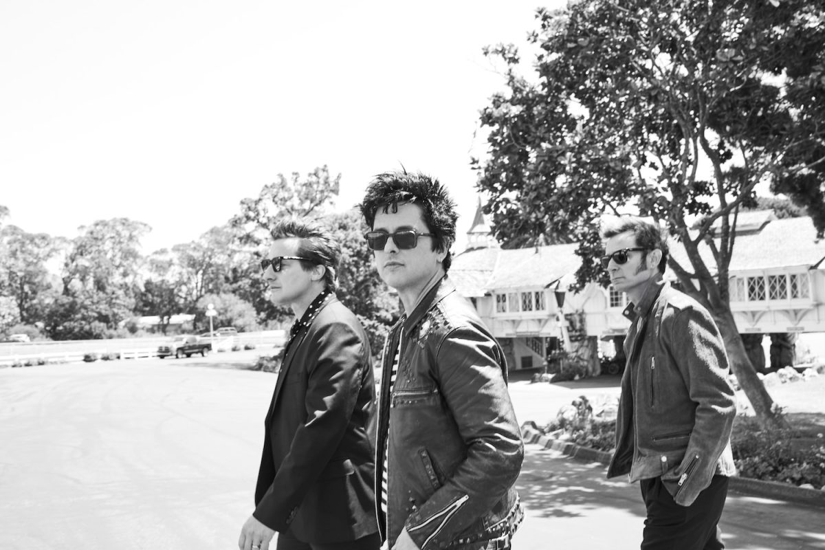 A black-and-white photograph of three men walking down the street in front of a house.